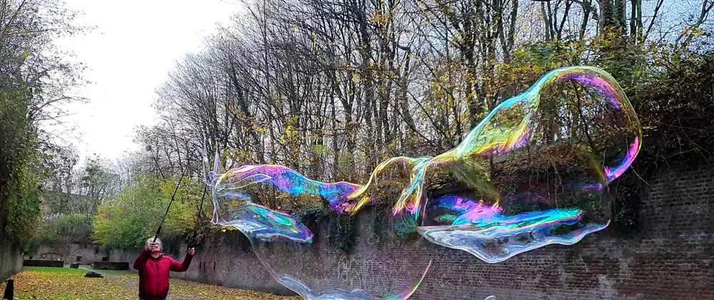 Une personne crée de grosses bulles de savon dans un parc verdoyant.