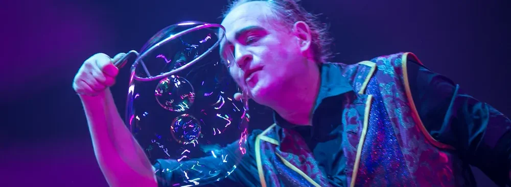 Magicien jouant avec une grosse bulle de savon, lumière magenta en arrière-plan.