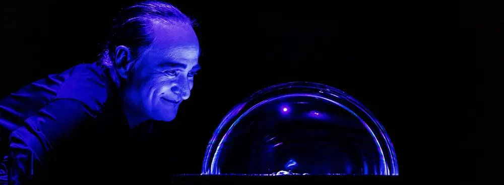 Homme dans une pièce sombre, sous une coupole lumineuse, souriant et plein d’attente.