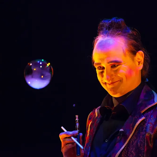 Un clown sourit en tenant une bulle de savon et un porte-cigarette.